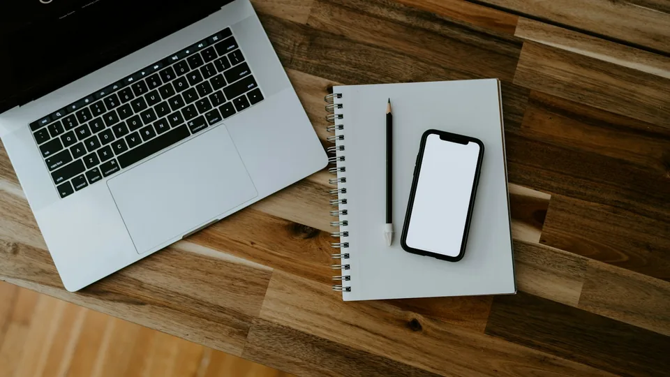 A laptop and smartphone on a desk, representing the connected devices used with productivity apps.